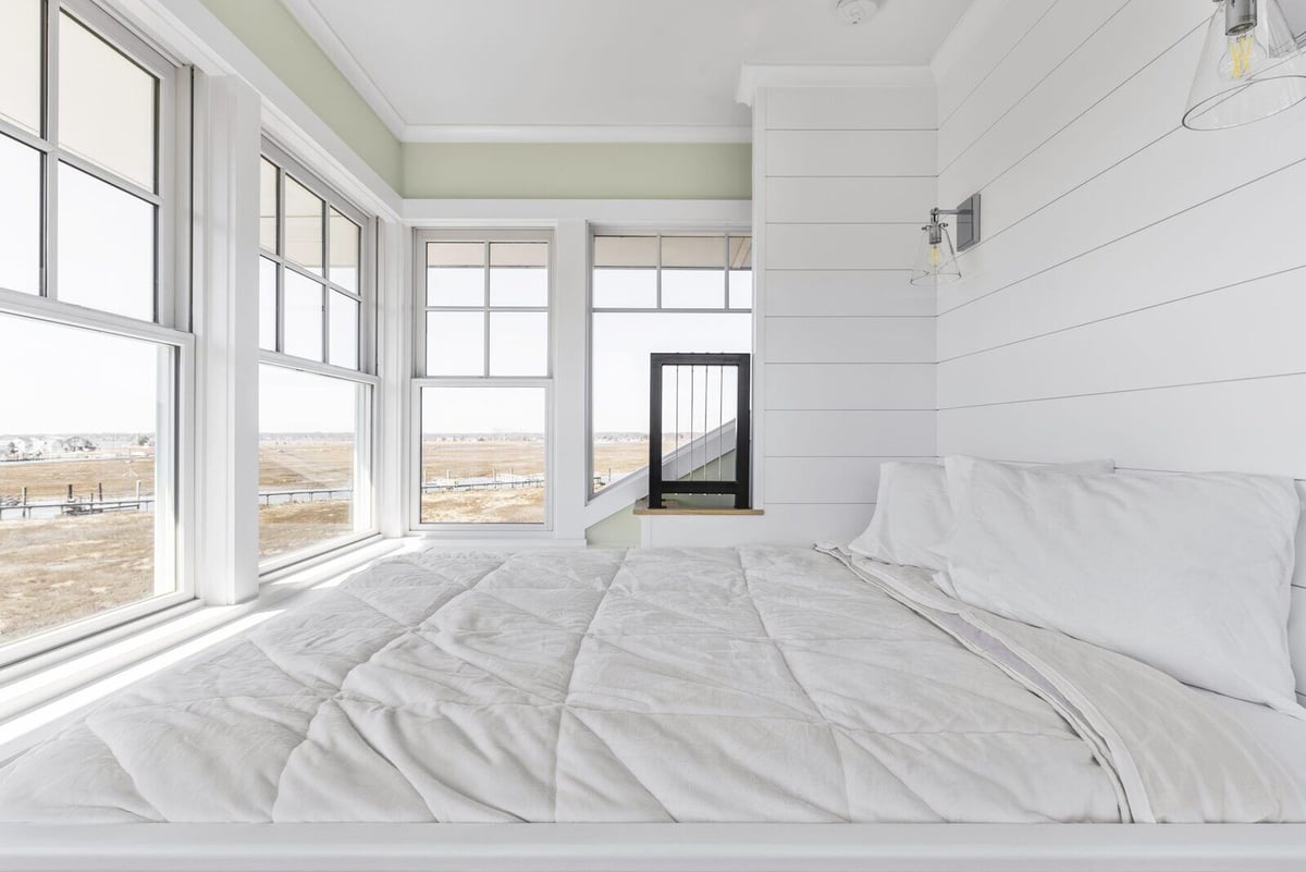 Bright bedroom with panoramic windows and a custom white bed in Essex, Connecticut by Craft Design + Build