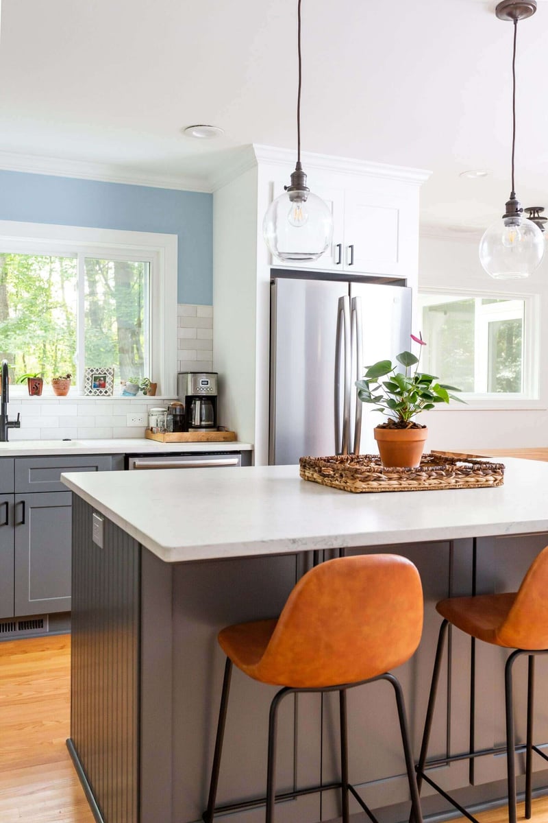 Contemporary kitchen with white countertops and brown leather stools in an Essex remodel by Craft Design + Build