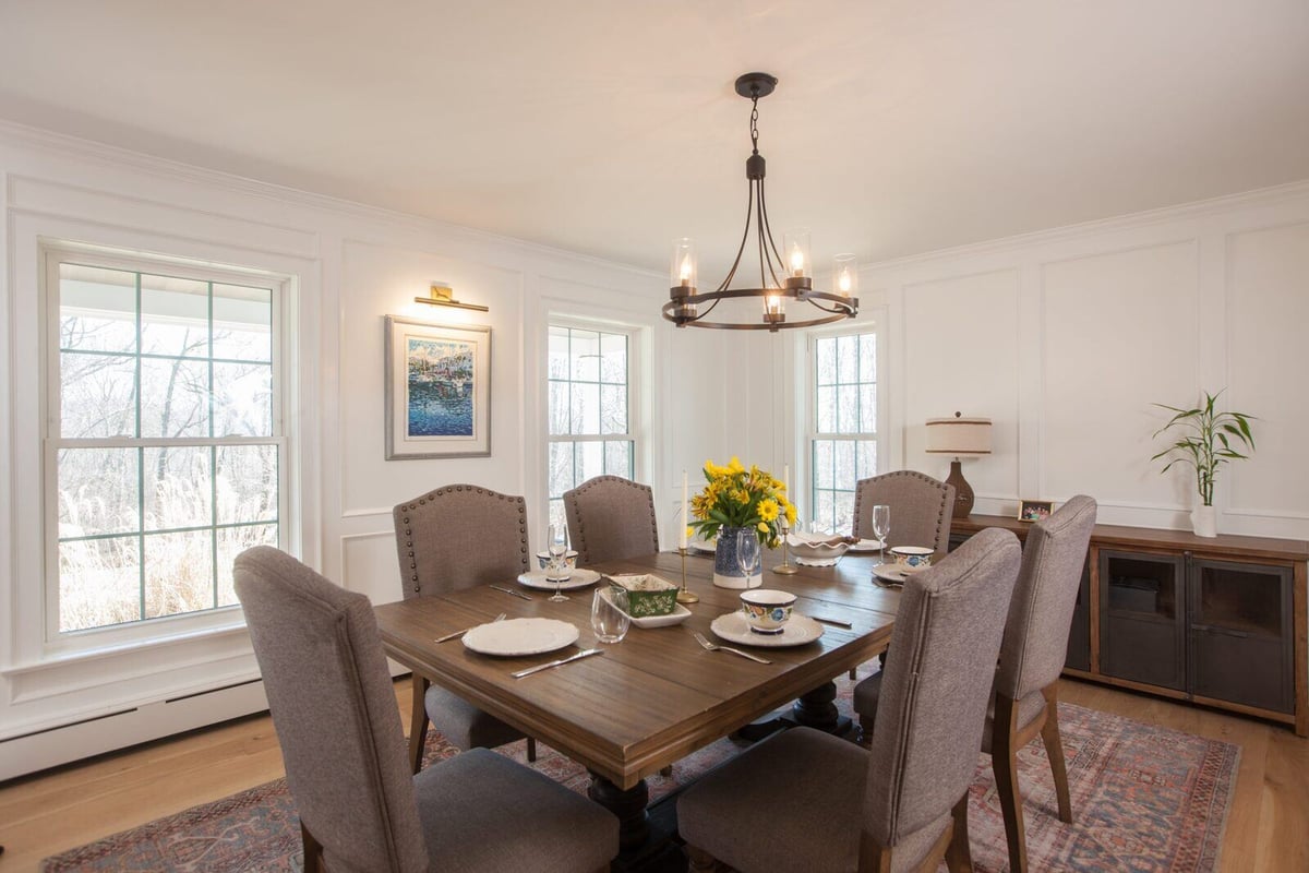 Dining room with large windows, wooden dining set, and chandelier, located in an Essex, Connecticut farmhouse