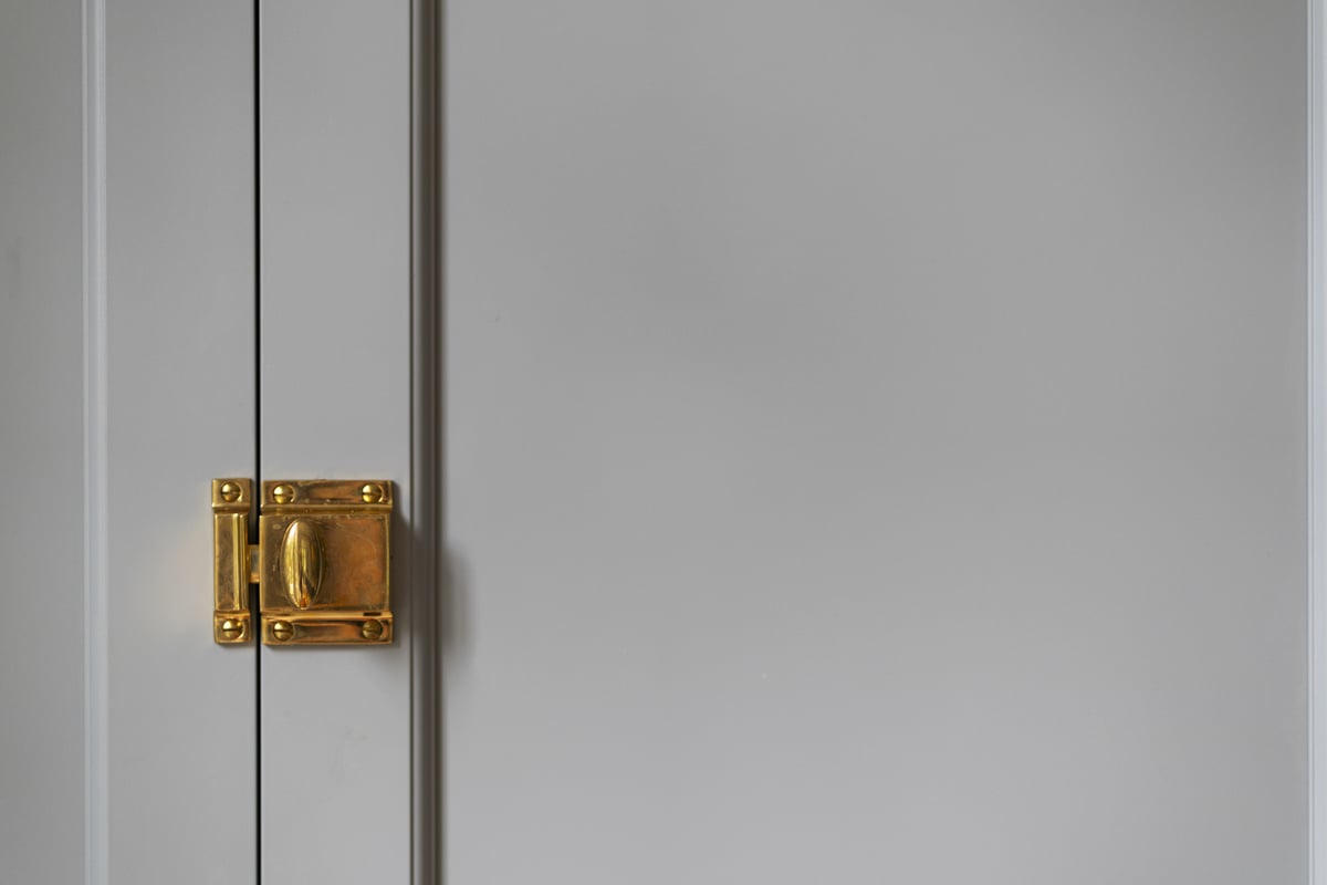 Close-up of gold latch on grey kitchen cabinets, remodeled by Craft Design and Build in Essex, Connecticut