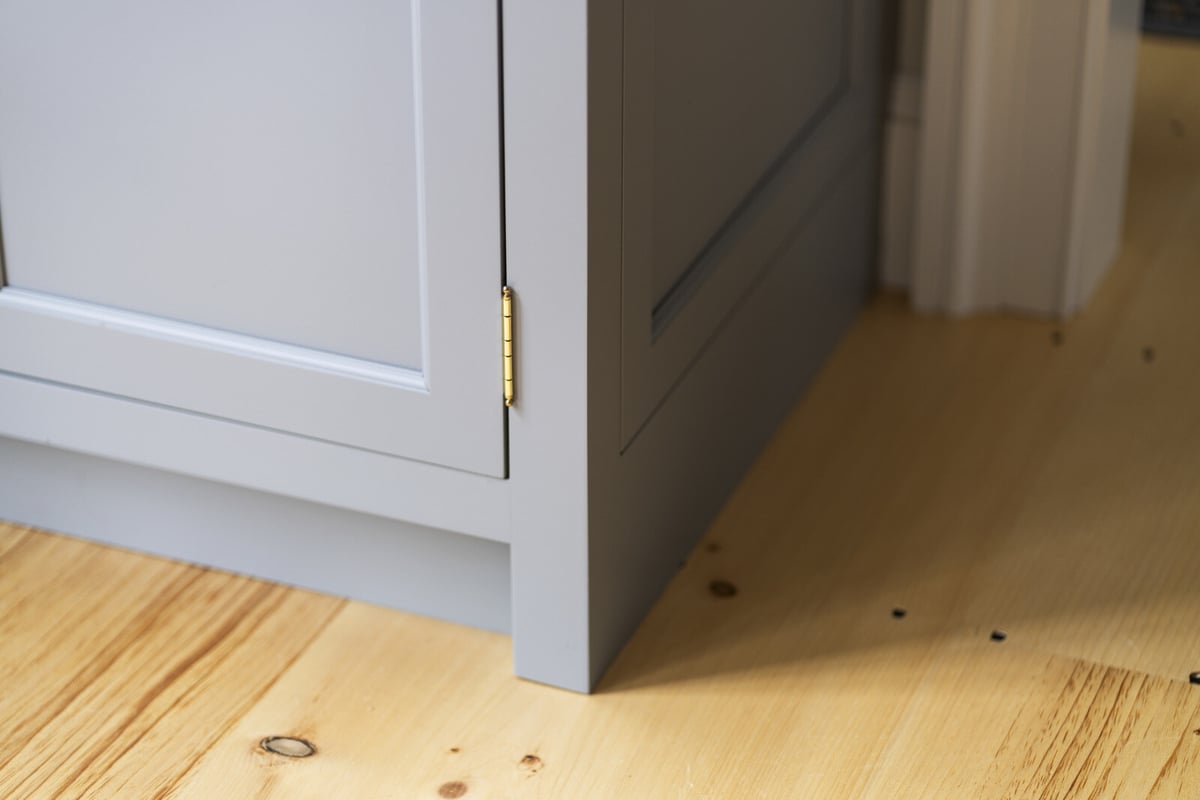 Close-up of kitchen cabinet base with gold hinge, remodeled by Craft Design and Build in Essex, Connecticut