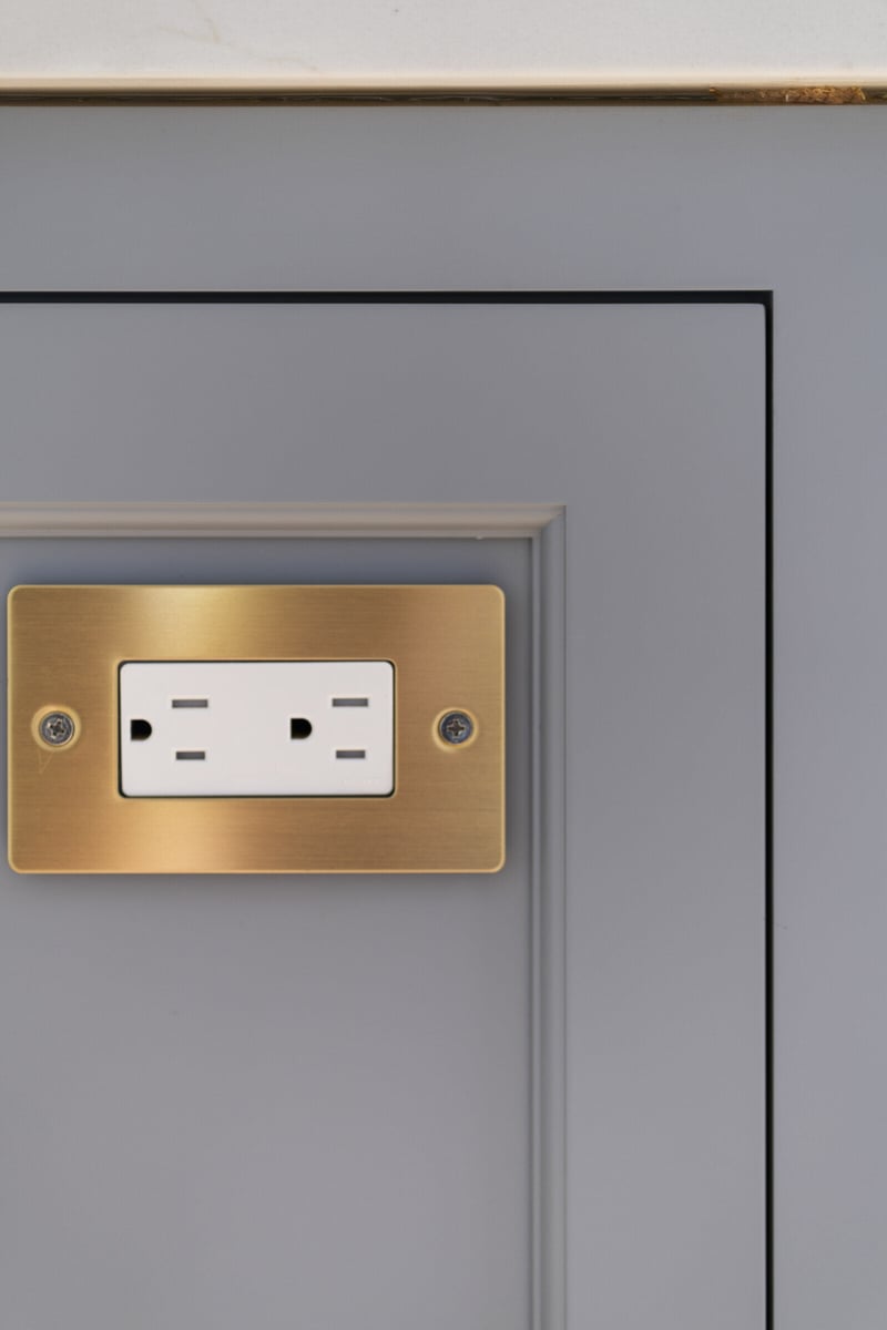 Electrical outlet with gold plate on grey kitchen island, remodeled by Craft Design and Build in Essex, Connecticut