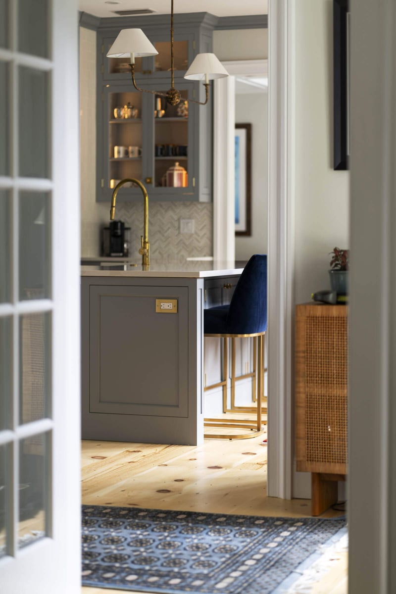 View of kitchen with grey cabinets and gold fixtures through doorway, designed by Craft Design and Build in Essex, Connecticut