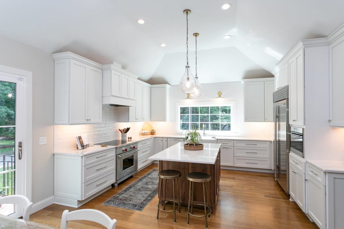 Full view of a white and wood kitchen with a central island and glass pendant lights in a remodeled Essex, Connecticut home