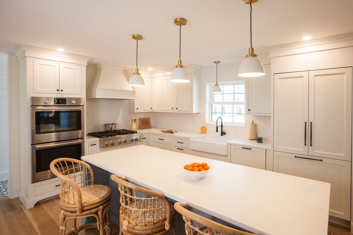 Kitchen with a large island, white cabinetry, and wood flooring in a Clinton Farmhouse by Craft Design + Build