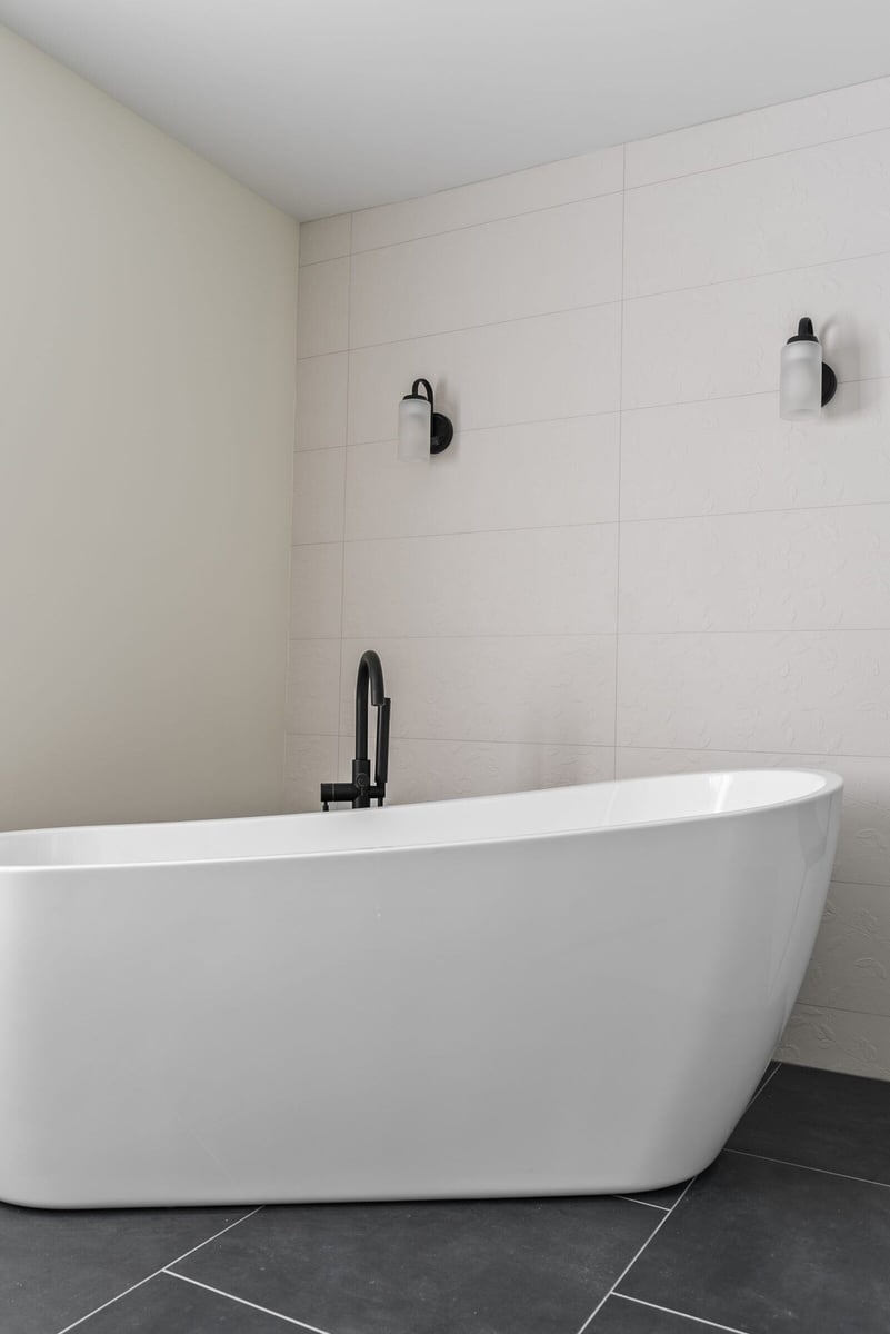 Minimalist bathroom with a white tub and black fixtures, part of a Killingworth renovation by Craft Design + Build