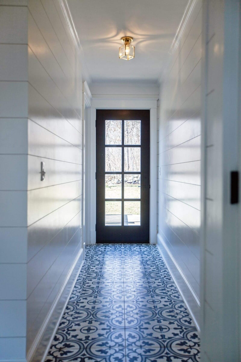 Sunlit hallway featuring shiplap walls and decorative floor tiles ending in a glass door with outdoor view