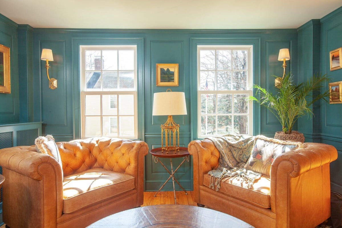 Sunlit sitting area with leather armchairs and teal paneled walls in a Chester, Connecticut remodel by Craft Design + Build