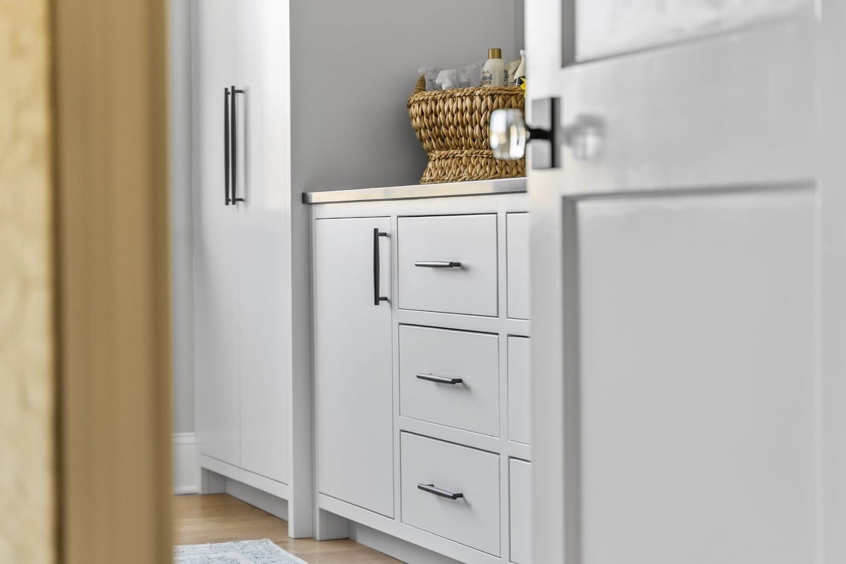 White cabinetry and woven basket in a well-organized Essex laundry room by Craft Design + Build, Essex Connecticut