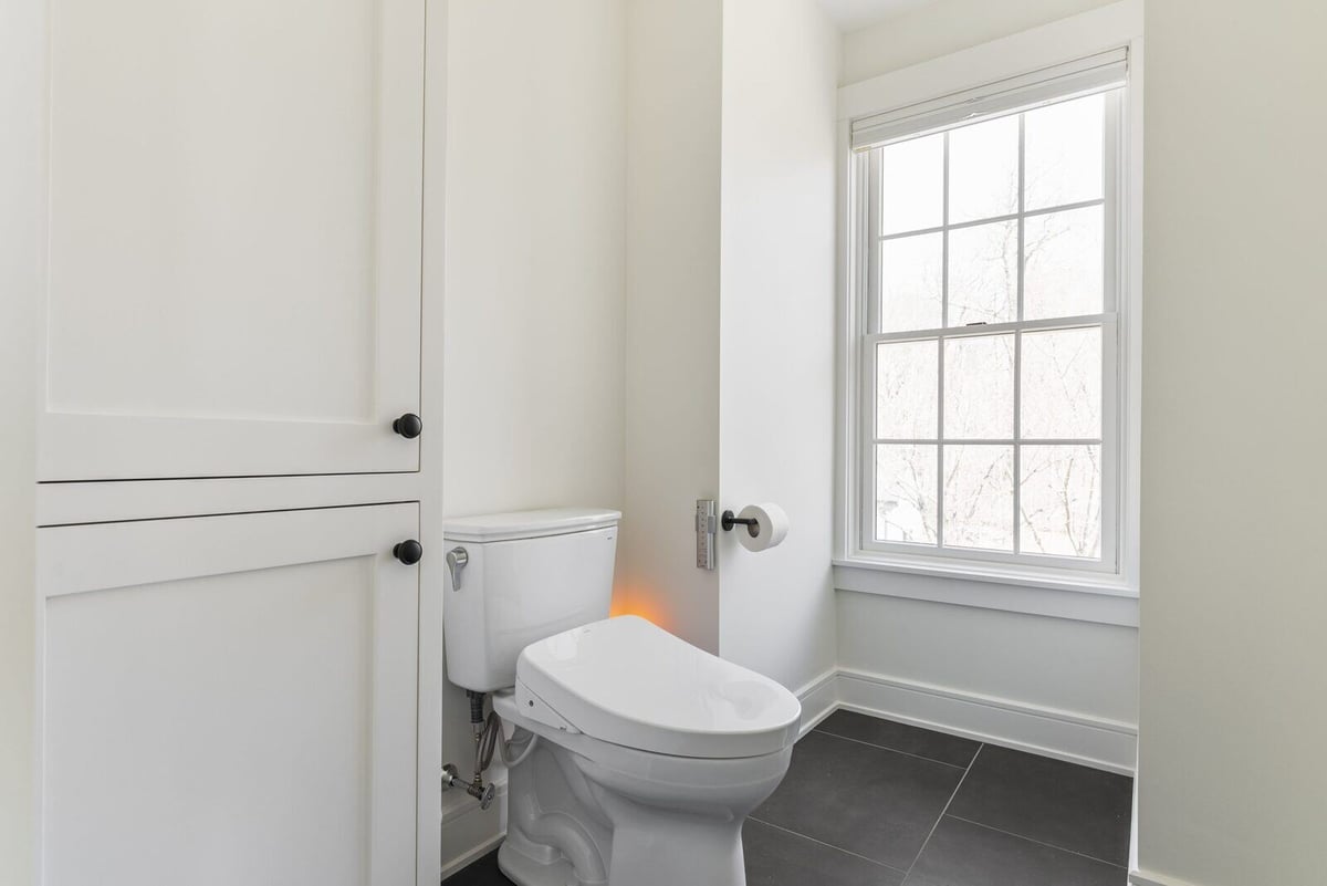 White toilet and large window in a clean, modern bathroom in Killingworth, designed by Craft Design + Build, Essex, Connecticut